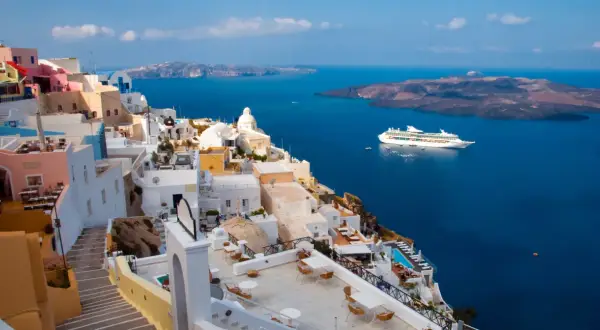 Santorini, Grecja. Białe domy na klifie, błękitne morze i statek wycieczkowy. Planujesz podróż? Pamiętaj o podatku turystycznym Grecja.