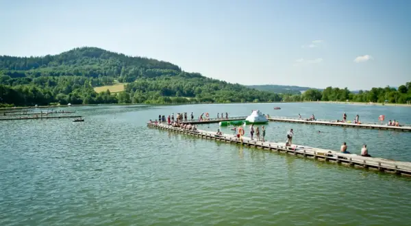 Ludzie odpoczywają na drewnianych pomostach nad jeziorami Dolnego Śląska. W tle zielone wzgórza.