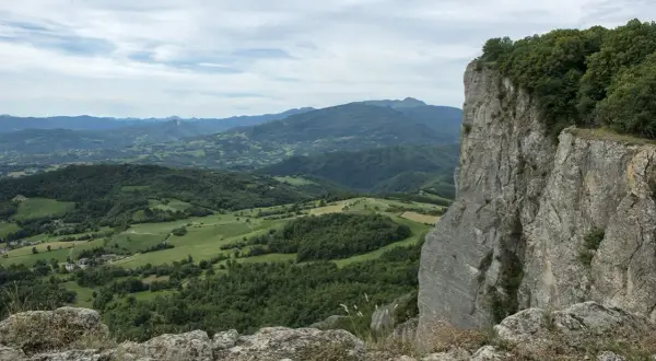 Vista panoramica dalla cima della Pietra di Bismantova, con colline verdi e montagne all'orizzonte sotto un cielo nuvoloso.