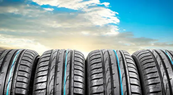 Quatre pneus de voiture, parfaits pour l'été ou toutes saisons, alignés sous un ciel bleu éclatant avec des nuages blancs.