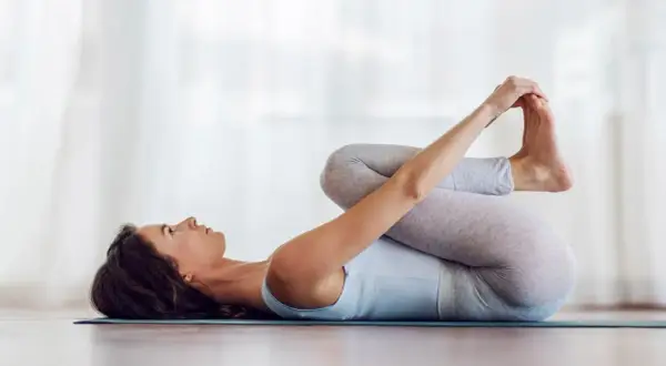Mujer en postura del bebé feliz, abrazando sus pies con las manos, relajada en una esterilla de yoga.