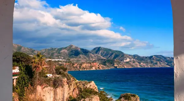Vue panoramique de la côte andalouse, parfaite pour un guide Malaga. Falaises rocheuses, mer bleue et montagnes verdoyantes sous un ciel d'azur.