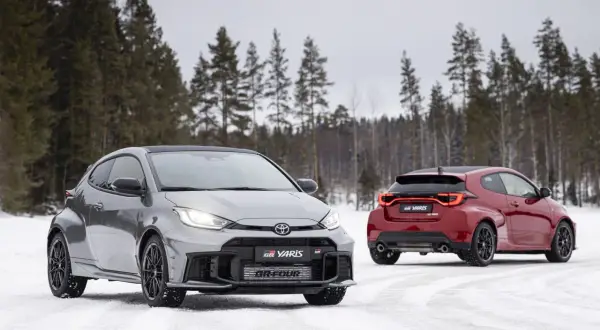 Dwa sportowe toyoty hatchback GR Yaris na śniegu, jeden szary z przodu, drugi czerwony z tyłu, na tle zimowego lasu.