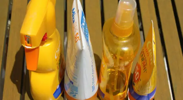 Prodotti solari scaduti, tra cui una crema solare spray e una lozione, pronti per essere smaltiti. Dove si buttano le creme scadute?
