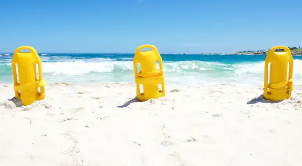 Trzy żółte bojki ratownicze stoją na piaszczystej plaży, z morzem i niebem w tle.