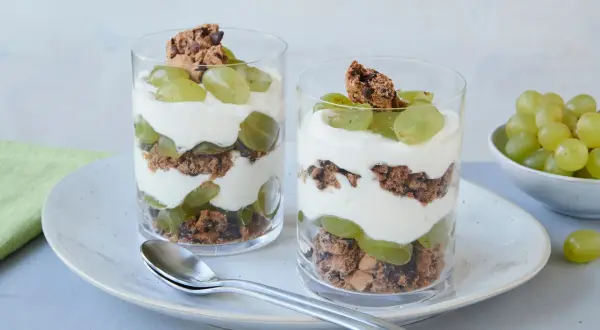 Zwei Gläser mit einem leckeren Trauben-Cookie-Dessert, geschichtet mit Joghurt und Keksbröseln.
