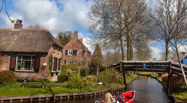 Paseo en barca por los canales de Giethoorn, Holanda, con casas de tejado de paja y un puente de madera.