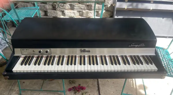 A vintage Fender Rhodes Stage Piano Mark I, a classic among labs vintage keys, sits on a teal metal stand outdoors.