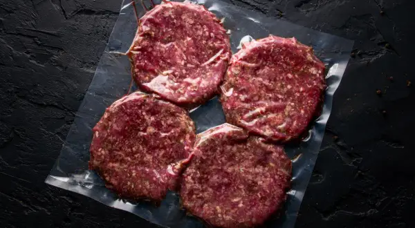 Cztery surowe kotlety na hamburgery w folii. Zastanawiasz się, mięso na hamburgery jak przyprawić?