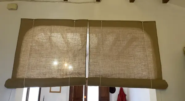 Dos estores enrollables caseros de tela rústica cubren una ventana y una puerta.