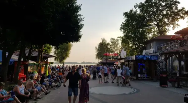 Tłum ludzi spaceruje promenadą w Skorzęcinie, korzystając z licznych atrakcji i letniej atmosfery nad jeziorem.