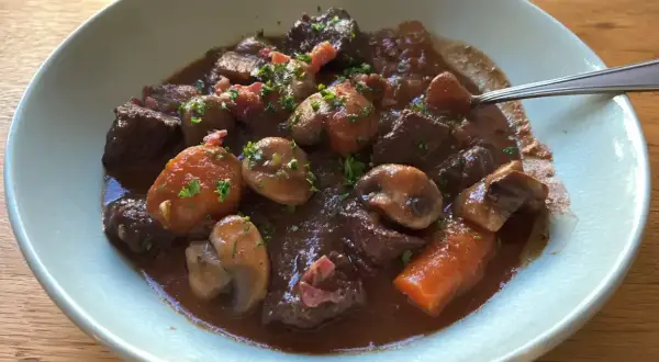 En mustig boeuf bourguignon med möra köttbitar, champinjoner och morötter i en djup rödvinssås, toppad med persilja.