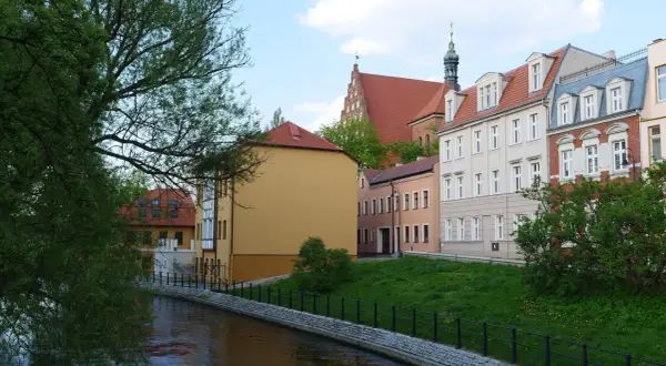 Nad rzeką malownicze kamienice. Chcesz wiedzieć, jak sprawdzić czy budynek jest w rejestrze zabytków? Spójrz na detale architektoniczne i wieżę kościelną.