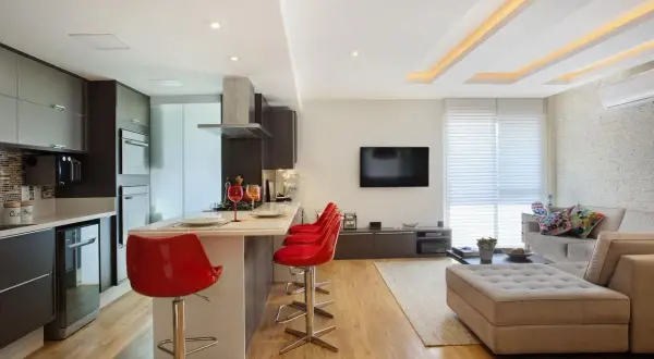 Elegante cucina moderna con isola e sgabelli rossi, separata dal soggiorno da un pratico cartongesso divisorio.