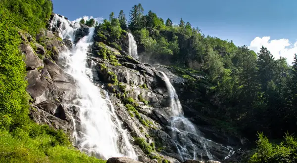 Le Cascate Nardis, un imponente salto d'acqua che scende su rocce scure, circondate da un verde lussureggiante e alberi imponenti sotto un cielo azzurro.