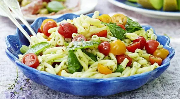 En härlig pastasallad vegetarisk med körsbärstomater, basilika och pinjenötter i en blå skål.