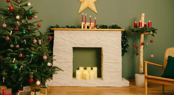 Festliche Szene mit geschmücktem Weihnachtsbaum, selbstgebauter Kaminkonsole, Kerzen und Geschenken.