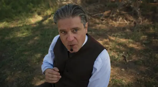 Un uomo con un sigaro in bocca, vestito elegantemente, sembra un re.