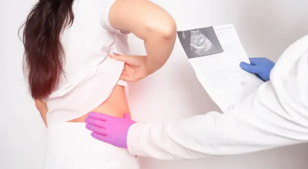 Lekarz w niebieskiej rękawiczce trzyma wyniki badań, podczas gdy pacjentka w białej koszulce odsłania bok. To ilustracja, jak wygląda badanie urologiczne u mężczyzn.