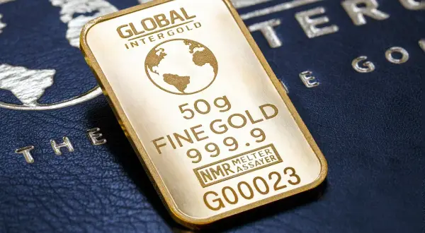 Sztabka złota 50g, czyli ok. 1.6 uncji, z napisem "FINE GOLD 999.9". Na tle ciemnej skóry z wytłoczonym globusem.