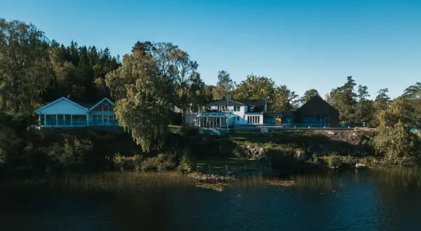 Hällsnäs Hotell & Restaurang vid en sjö, omgivet av träd. En vacker plats för avkoppling och god mat.