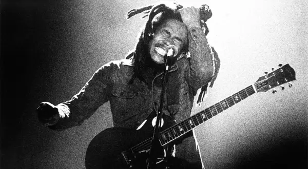 Bob Marley z gitarą, w transie, śpiewa na scenie. Jego dredy unoszą się w powietrzu, a ręka sięga do głowy. To ikona muzyki, której rytmy ska porwały tłumy.