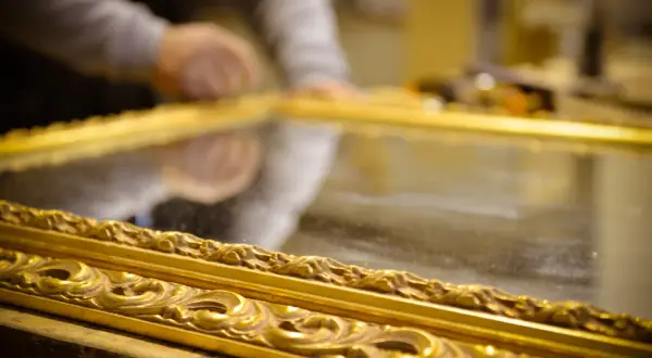 Mani esperte al lavoro per il restauro specchio antico. La cornice dorata e intarsiata riflette la cura del dettaglio.