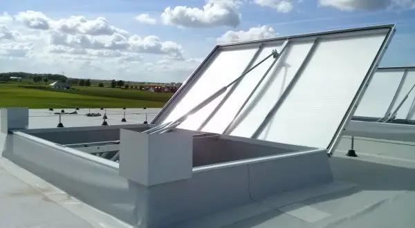 Otwarta klapa dymowa na dachu, z widokiem na zielone pola i błękitne niebo z chmurami.