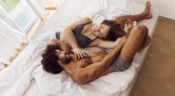 Para, która leży na łóżku, śmieje się i dotyka. To obraz tego, co to seksualność: bliskość, intymność i radość.