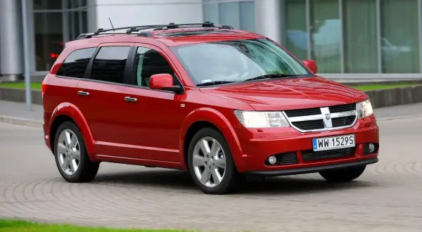 Czerwony Dodge Journey 3.6 z relingami dachowymi jedzie po brukowanej drodze.