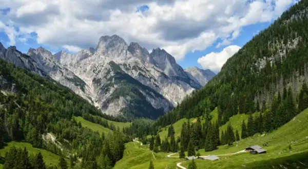 Grüne Almwiesen und Nadelwälder schlängeln sich zu majestätischen Berggipfeln. Kleine Hütten und Pfade deuten auf Berchtesgaden Geheimtipps hin.