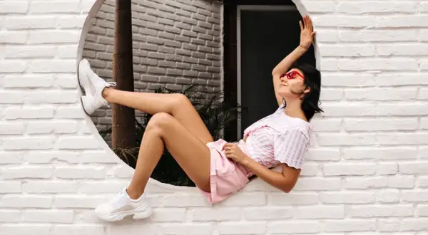 Ragazza con occhiali rossi e cljd scarpe bianche, sdraiata su un davanzale bianco.