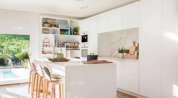 Elegante mueble cocina isla blanco con taburetes, encimera de cuarzo y vistas a un jardín con piscina.