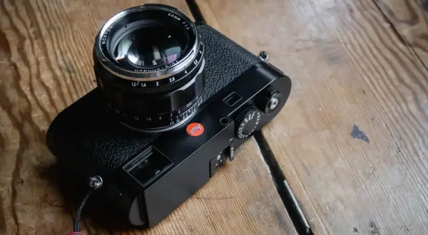A black Leica M262 camera with a Nokton 50mm f/1.2 lens sits on a wooden surface.