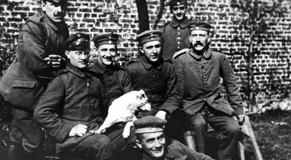 Grupp soldater i uniform, en håller en vit hund. En av männen liknar en ung Hitler.