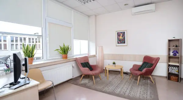 Jasne, przytulne wnętrze gabinetu psychologicznego z dwoma różowymi fotelami i stolikiem.