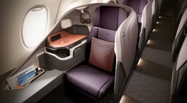 Luxuriöser Sitzbereich in der **besten Business Class** mit lila Ledersitzen, Kissen und einem Fenster.