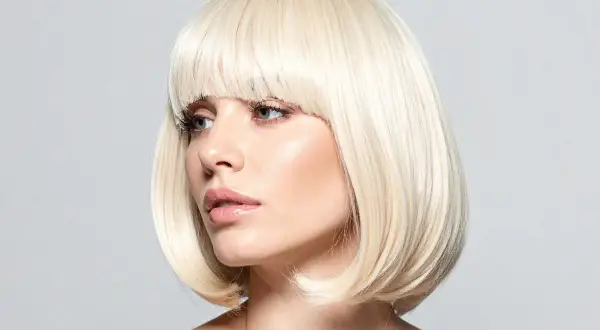 Blond cieniowany bob fryzura z grzywką. Kobieta z delikatnym makijażem patrzy w bok.