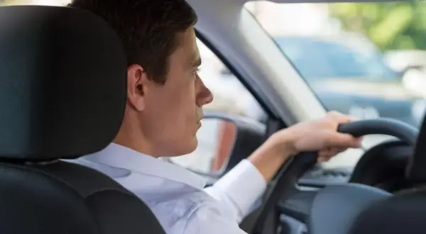 Uomo al volante, con la mano sul volante. Si può guidare una macchina intestata ad un familiare, anche se non è la sua.