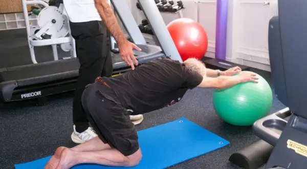 Un homme fait des exercices pour soulager son arthrose lombaire, guidé par un kinésithérapeute.
