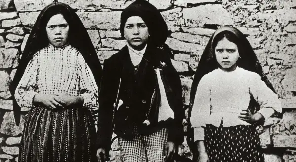 Trójka dzieci, w tym siostra Łucja z Fatimy, pozuje przed kamiennym murem.