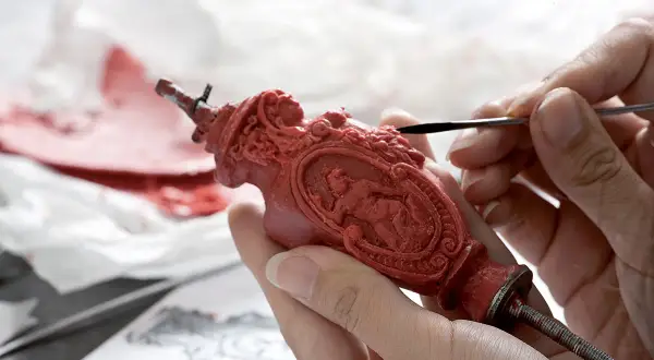 Mani esperte rifiniscono un oggetto in cera rossa, un'opera d'arte che ricorda la **fondazione Cologni**. Dettagli intricati prendono forma sotto gli strumenti.