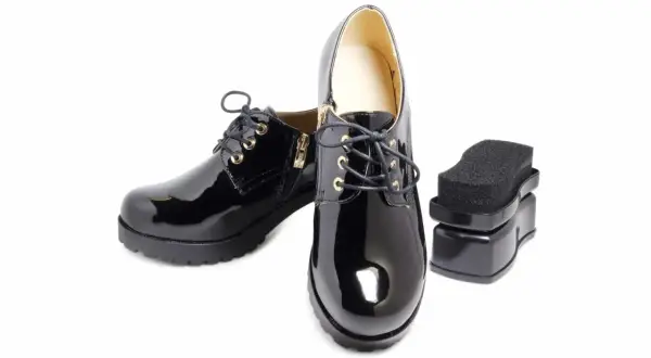 Paire de chaussures vernies synthétiques noires avec un applicateur de cirage. Parfait pour l'entretien des chaussures vernies synthétiques.