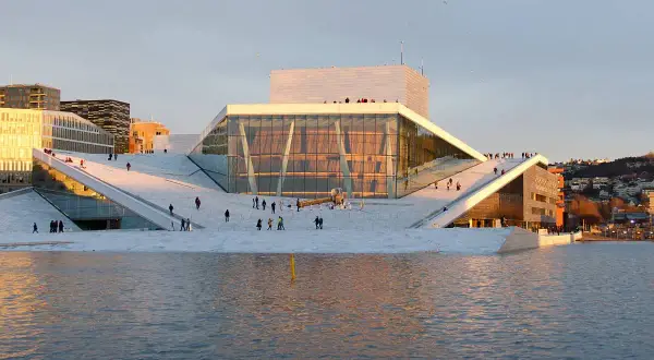 Oslo Winter: Menschen spazieren auf dem Dach der Oper, die im warmen Abendlicht glänzt.