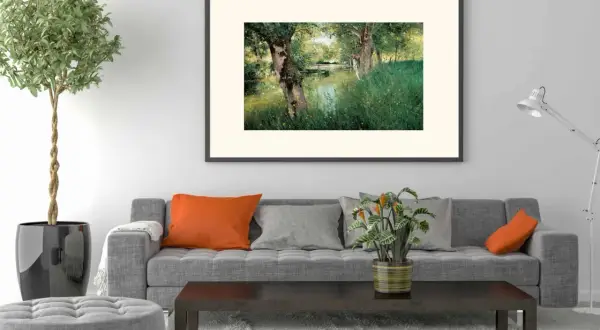 A modern impressionism painting of a serene riverbank with lush green grass and trees, framed above a grey sofa with orange and grey cushions.