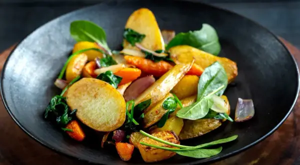 En tallrik med ugnsrostade rotfrukter, inklusive potatis, morötter och rödlök, blandat med färsk spenat. En härlig rotfrukter lista för en god måltid.