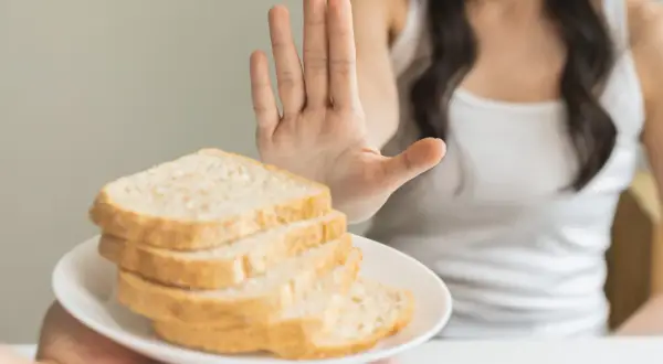 Osoba odrzuca talerz z chlebem, pokazując dłoń. To symbol walki z celiakią i unikania glutenu.