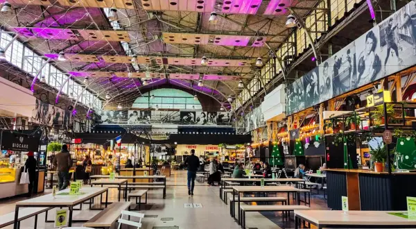 Wnętrze nowoczesnej vege restauracji w Warszawie. Widać stoły, ławki i stoiska z jedzeniem pod industrialnym dachem.