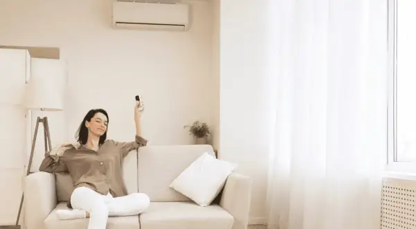 Mujer relajada en sofá con control remoto, pensando cuántas frigorías para 30 metros cuadrados necesita su hogar.