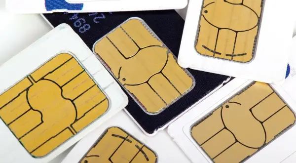 Zbliżenie na złote chipy kart SIM, ułożonych na białych plastikach i ciemnym tle. Każdy minisim gotowy do działania.